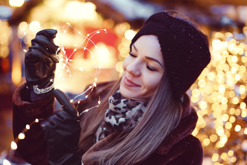 Young imaginative woman holding fairy lights in Christmas market