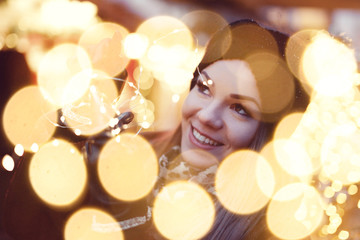 Obraz na płótnie Canvas Happy woman holding fairy light garland in bokeh outdoors in Christmas market