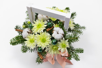 Fototapeta na wymiar arrangement of flowers (chrysanthemum light green), branches of fir, Christmas decorations (green), cotton flowers and a pink ribbon in a white wooden box