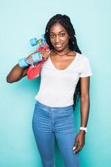 Portrait of african woman in trendy summer clothes and sunglasses with penny skateboard posing on blue background
