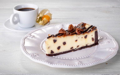 Brownie cheesecake with nuts on white plate next to cup of coffee. Close up.