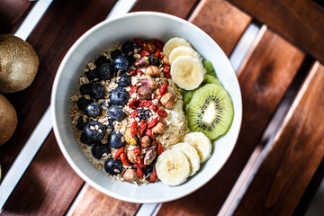 Top down view of a muesli bowl with yogurt, fruits and nuts on a wooden table