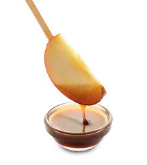 Dipping of apple wedge into glass bowl with sauce on white background