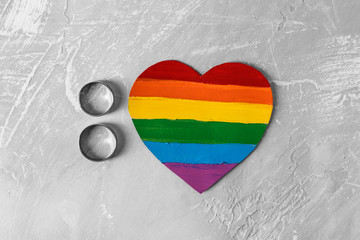 Rainbow heart with engagement rings on grey background. LGBT concept