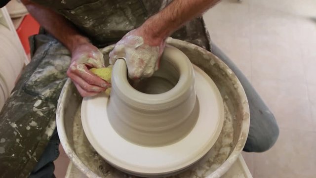 Artist potter in the workshop creating a jug out of earthenware, hands closeup. Twisted potter's wheel. Small aristic craftsmen business concept. 