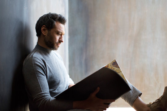 Junger Mann sitzt entspannt auf Treppe und liest in einer Zeitschrift