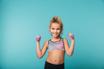 Smiling little sports girl doing exercises with dumbbells
