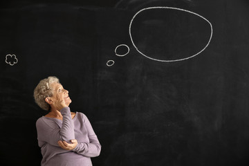 Senior woman near dark chalkboard with blank speech bubble
