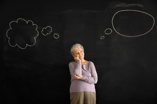 Thoughtful senior woman near dark chalkboard with blank speech bubbles