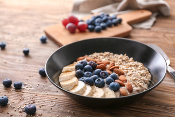 Tasty oatmeal with banana slices, blueberries and almonds on wooden table