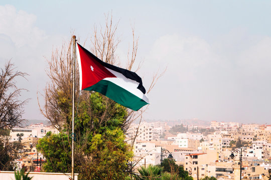 tricolor flag of Jordan on the background of the old poor of the city and blue sky.