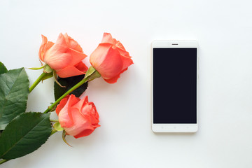 Top view of mobile phone with copy space and roses on white background. flat lay, mock up. Woman's workplace with phone and flowers.