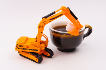 toy excavator loads cube sugar into a real cup of coffee on a light background