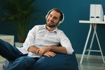 Fototapeta premium Young businessman with headphones sitting on beanbag chair in office