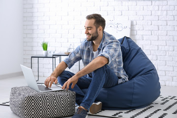 Young man with laptop sitting on beanbag chair at home
