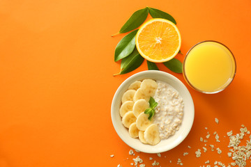Tasty oatmeal with banana slices in bowl and glass of orange juice on color table
