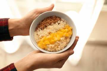 Woman holding bowl with tasty oatmeal and orange, closeup