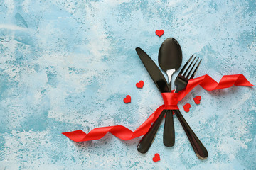 Cutlery with red ribbon and hearts on color background