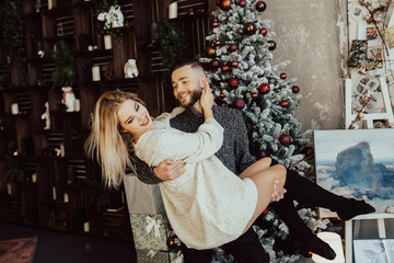 Happy young in love couple on Christmas tree background.Man holding in his arms his girl, girlfriend smiling.Love, family and valentines day concept. 