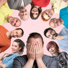 collage of different men and women showing positive emotions smiling and laughing on pink background. Man in the middle closing his face with hands. He is afraid that everybody scoff and mock on him.