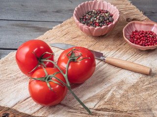 Three red tomatoes and multi-colored peppercorns in ceramic pink creamer wooden untreated stand
