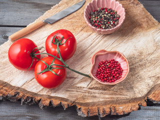 Red tomatoes on the sprigs, colorful pepper peas in a ceramic pink saucers on a wooden raw stand, kitchen knife.