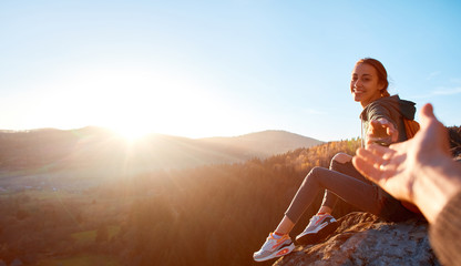 smiling woman hiker sits on edge of cliff against background of sunrise