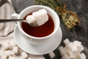 Adding of sugar to cup with aromatic tea on grey table