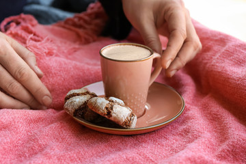 Woman taking cup of tasty aromatic coffee from plate with cookies