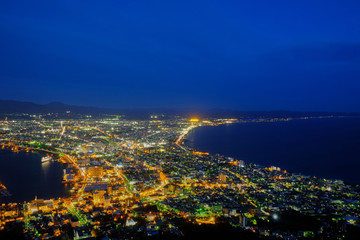 take a look city and harbor view point after sunset, see blue sky and light house at Mount Hakodate, Hokkaido, japan