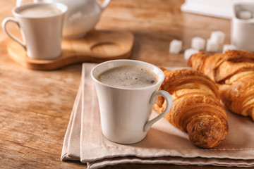 Cup of tasty aromatic coffee and croissants on wooden table