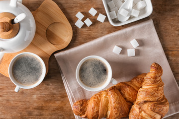 Cups of tasty aromatic coffee and croissants on wooden table