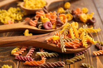 Spoons with different types of raw pasta on wooden table