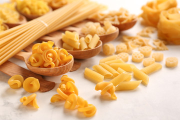 Spoons with different types of raw pasta on white table