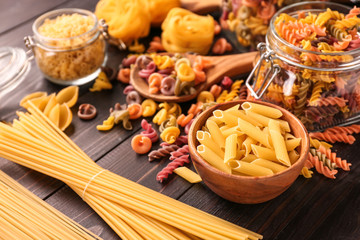 Different types of raw pasta on wooden table