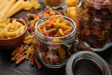 Jars with colorful raw pasta on wooden table