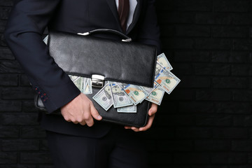 Businessman holding briefcase with dollar banknotes on dark background. Corruption concept