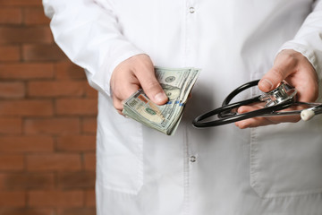 Doctor with bribe and stethoscope near brick wall, closeup. Corruption concept