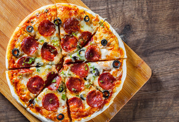 Pizza with Mozzarella cheese, pepperoni, tomato, pepper, olive, salami. Italian pizza on wooden table background