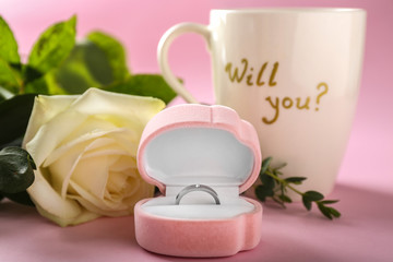 Box with beautiful engagement ring and rose on color background