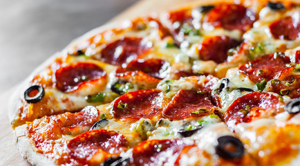 Pizza with Mozzarella cheese, pepperoni, tomato, pepper, olive, salami. Italian pizza on wooden table background