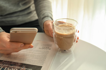 Woman with glass of tasty aromatic latte and mobile phone at light table