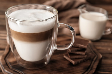 Glass cup of tasty aromatic latte on wooden board