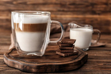 Glass cup of tasty aromatic latte on wooden board