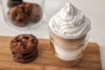 Glass of tasty aromatic latte with cookies on wooden board