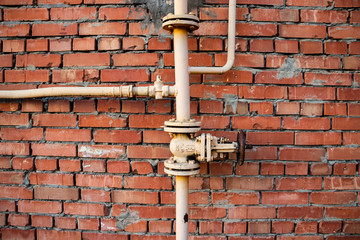 Gas pipes and a valve against a red brick wall.