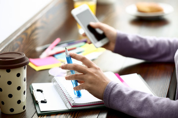 Woman with mobile phone and notebook sitting at table. Concept of study