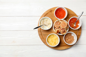 Set of tasty caviar with flapjacks on white wooden table