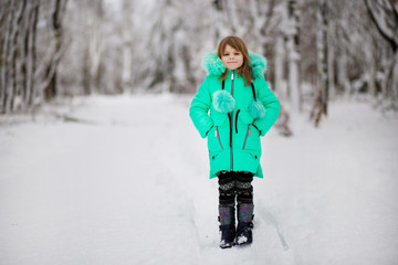 Fototapeta na wymiar Funny little girl having fun in beautiful park during snowfall