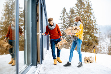 Young lovely couple dressed in colorful sweaters entering their modern home with firewoods in the...